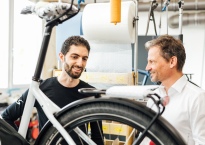 „Simplon Bikes“ komercijos direktorius Markus Geigeris (dešinėje) kalbasi su gamykloje dirbančiu pabėgėliu Abdeliu, EK nuotr.